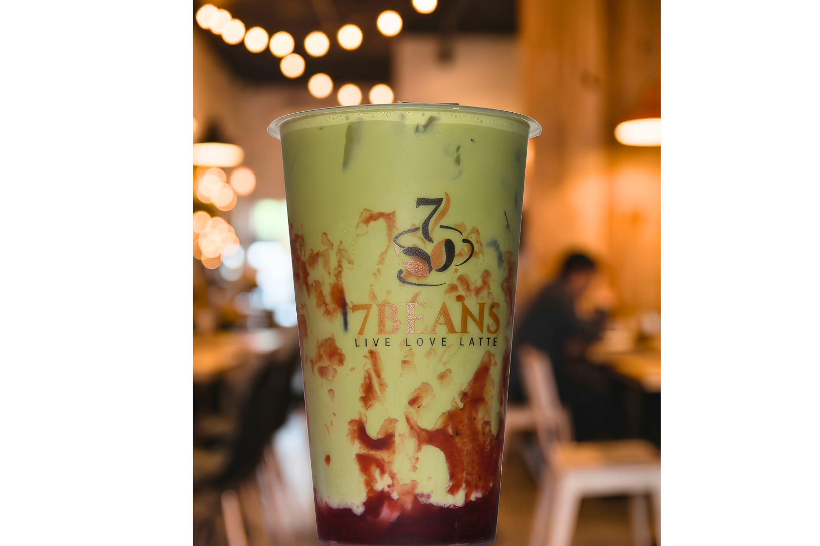 Strawberry matcha drink in a 7 Beans cup with warm café lights in the background